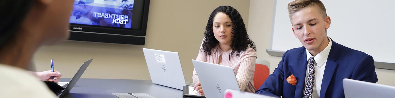 穿着商务服装的学生在会议室的桌子上工作. 东南科技的图像显示在屏幕上.