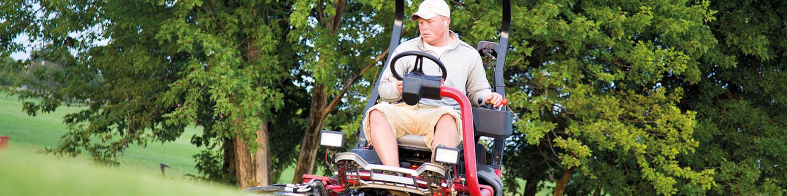 一名男子骑着大型割草机，在高尔夫球场上修剪草坪.