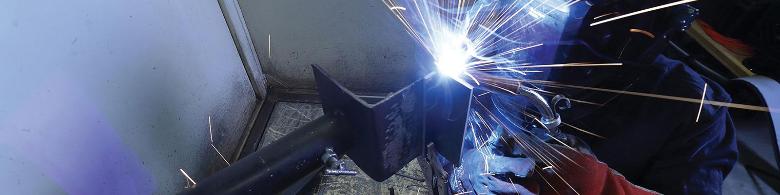 Side view of a Southeast Tech student in welding gloves and mask using a torch on a weld.